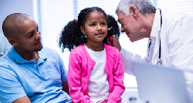 Doctor examining girl's ear while she sits on dad's lap