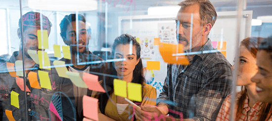 office people looking at a glass window with post-it notes- 550x245
