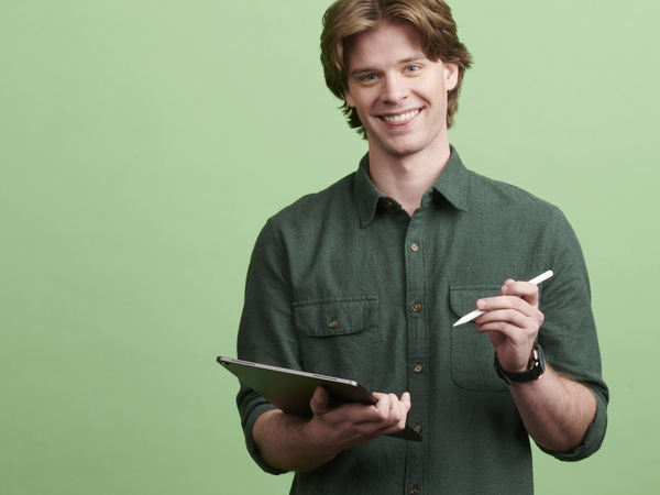 Young man smiling while holding a pen and note pad