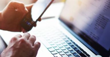 man holding phone and typing on laptop