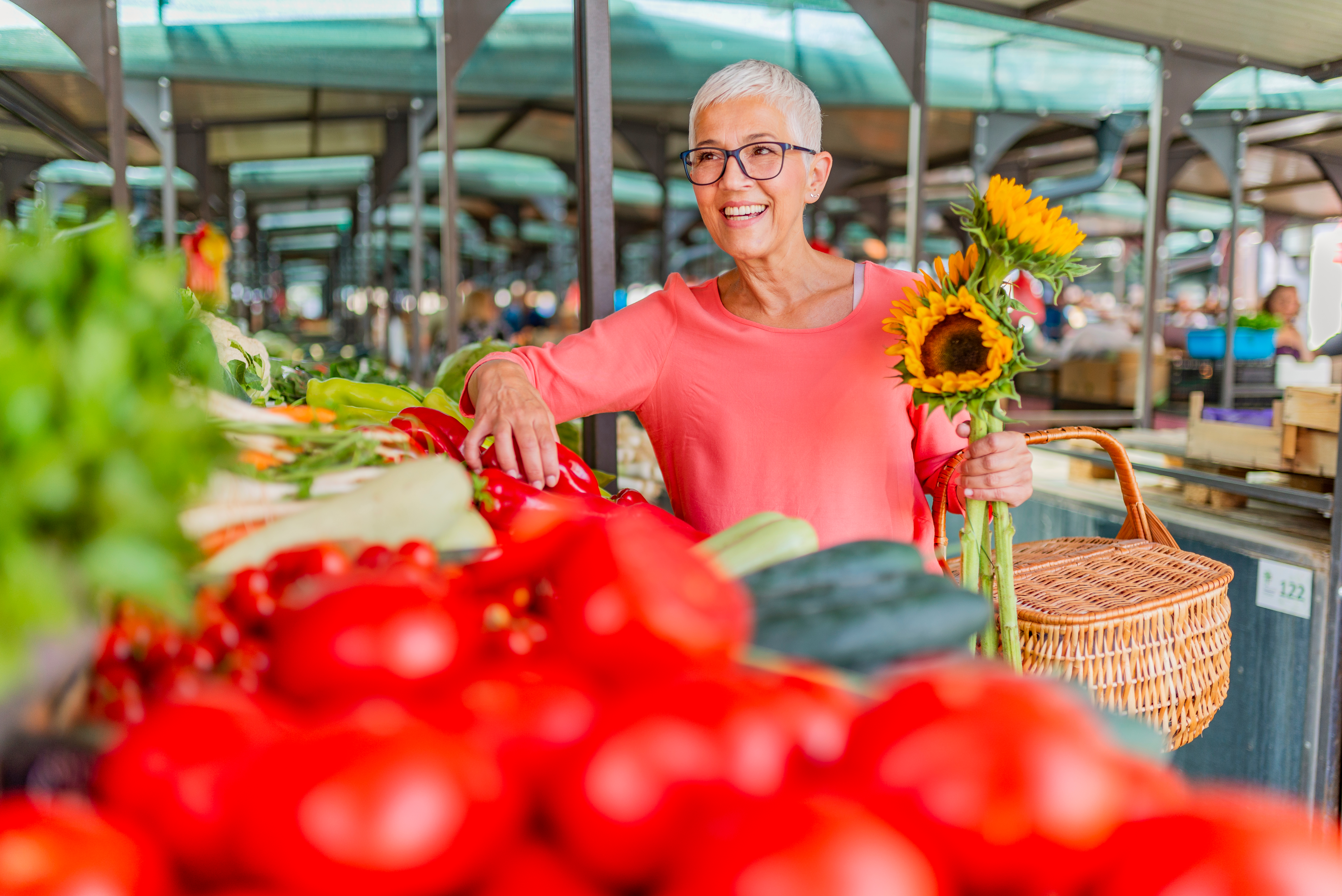 A women with a basket of sunflowers browsing the produce section at a grocery store.